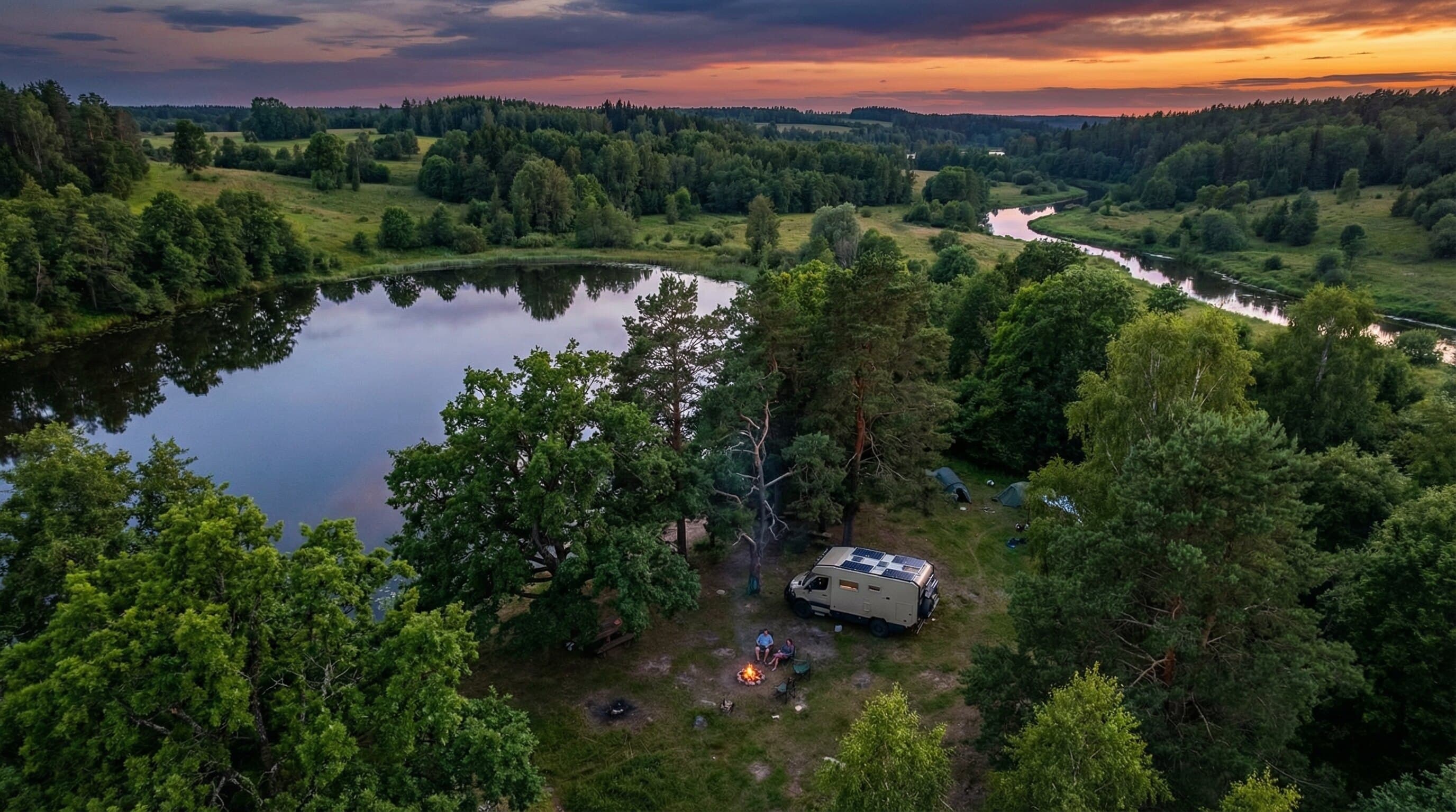 Aerial view of a campervan parked beside a forest lake at sunset